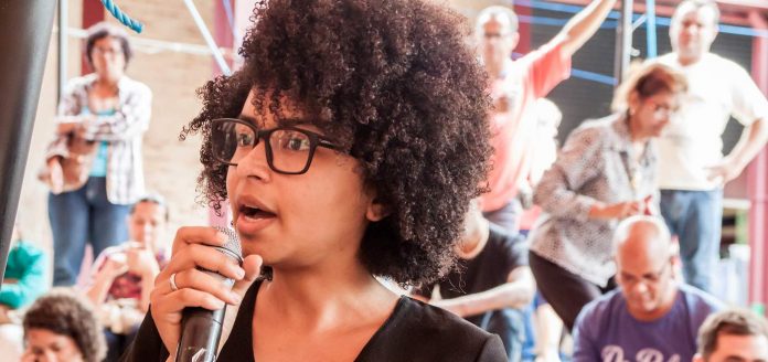 black woman at microphone debate-cc-Eu Governo