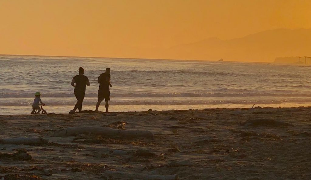 couple runs on beach with toddler keeping up on a bike