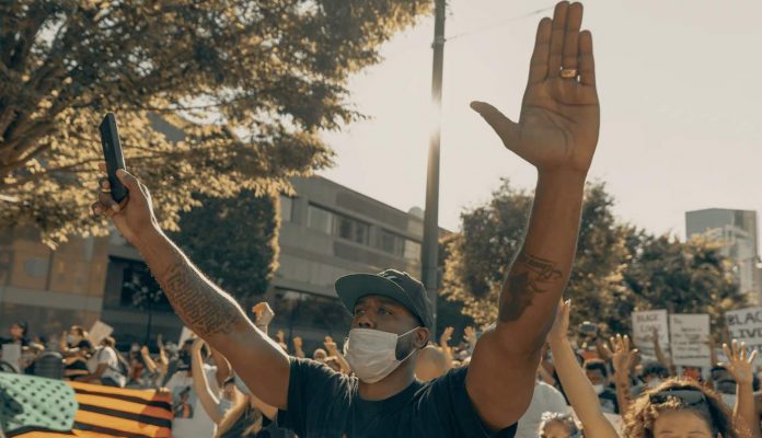 face mask on black protestor w hands up-pubdomain-Clay Banks